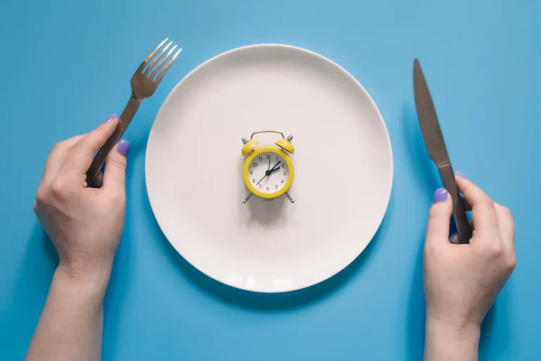 hands holding knife fork alarm clock plate blue background