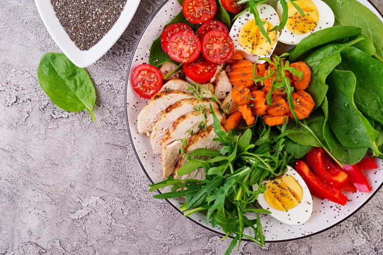 plate with keto diet food cherry tomatoes chicken breast eggs carrot salad with arugula spinach keto lunch top view (1)