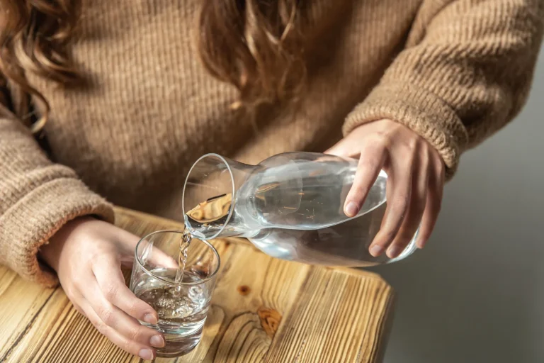 woman pours water into glass from glass decanter